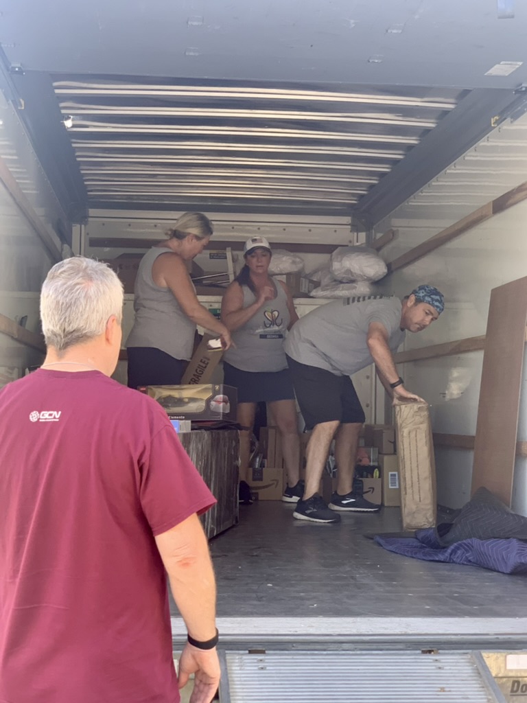 Volunteers unloading furniture and boxes from a moving truck during a transformation.