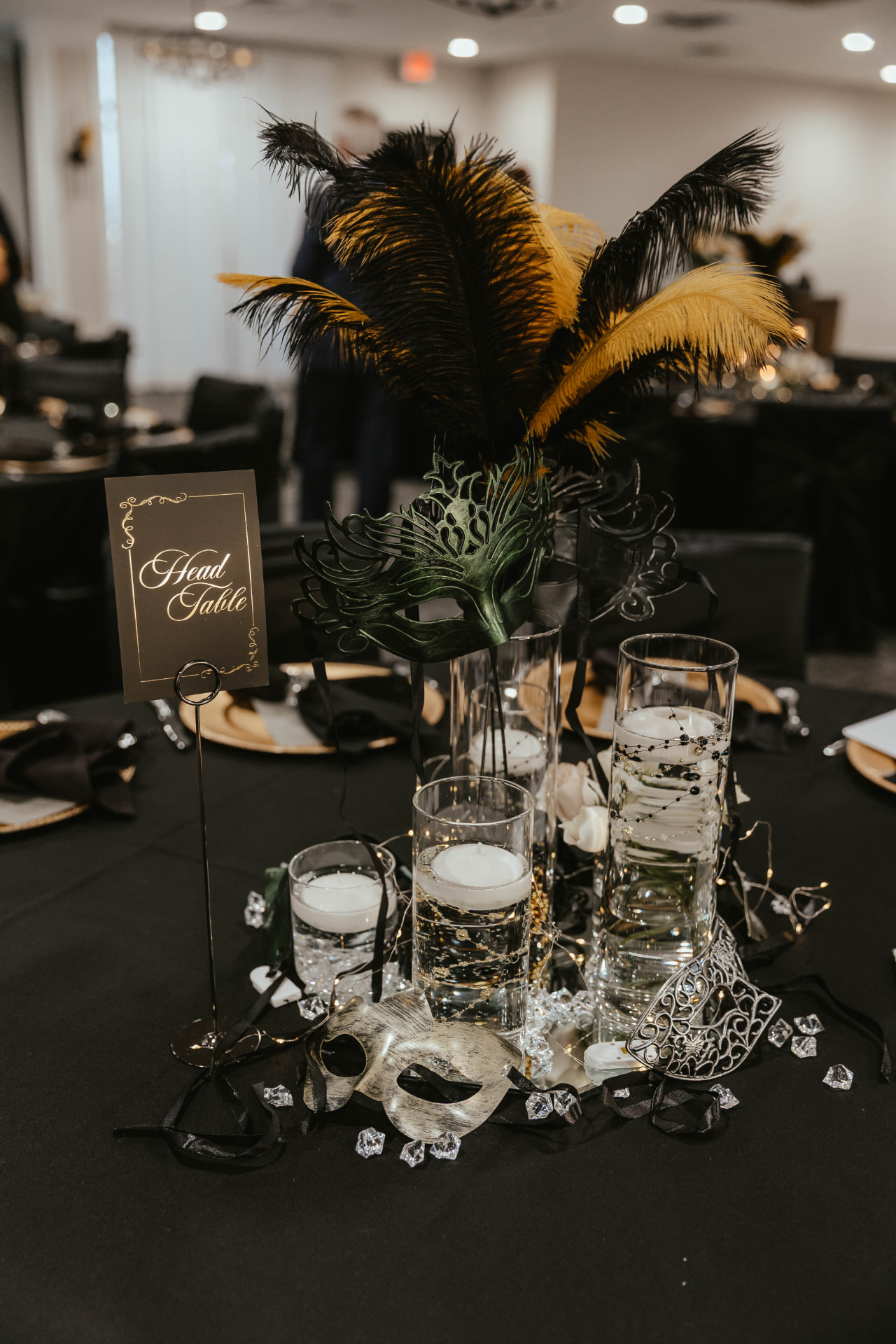Head table centerpiece with black and gold feathers, masquerade masks and candles.
