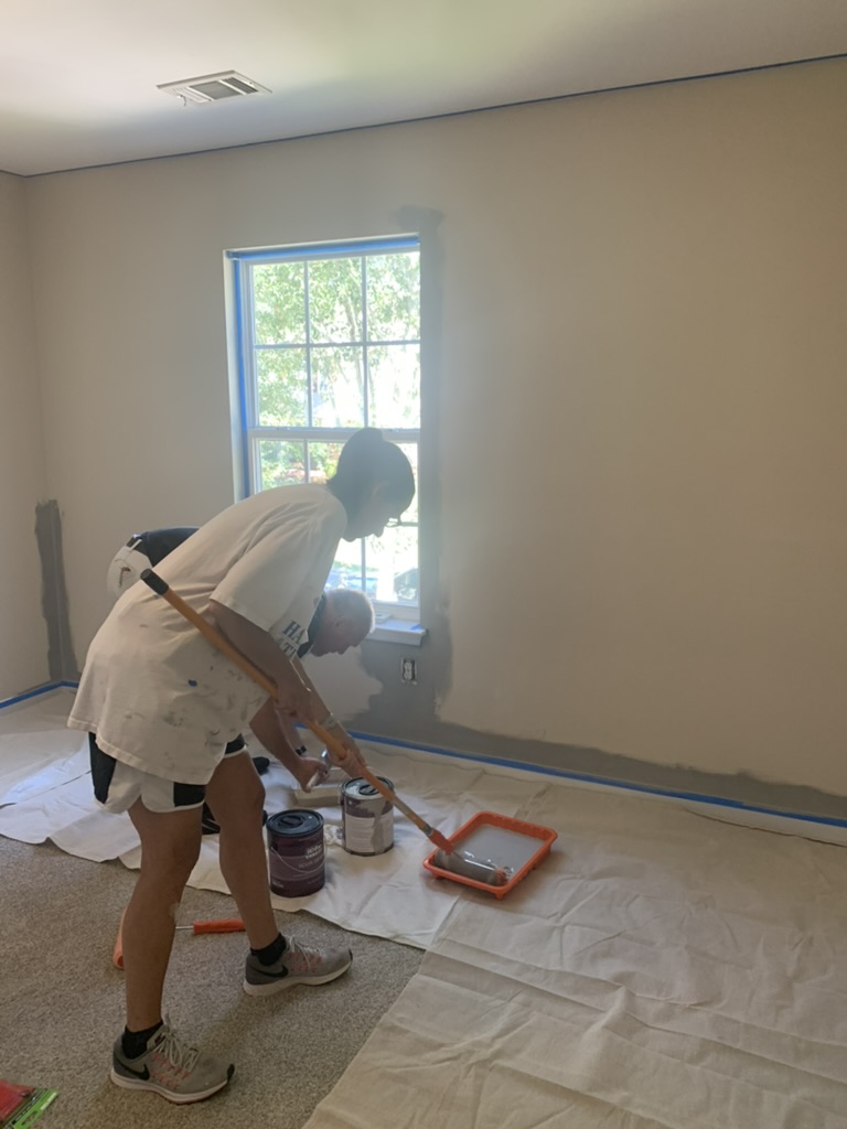 Volunteer rolling gray paint onto a bedroom wall.