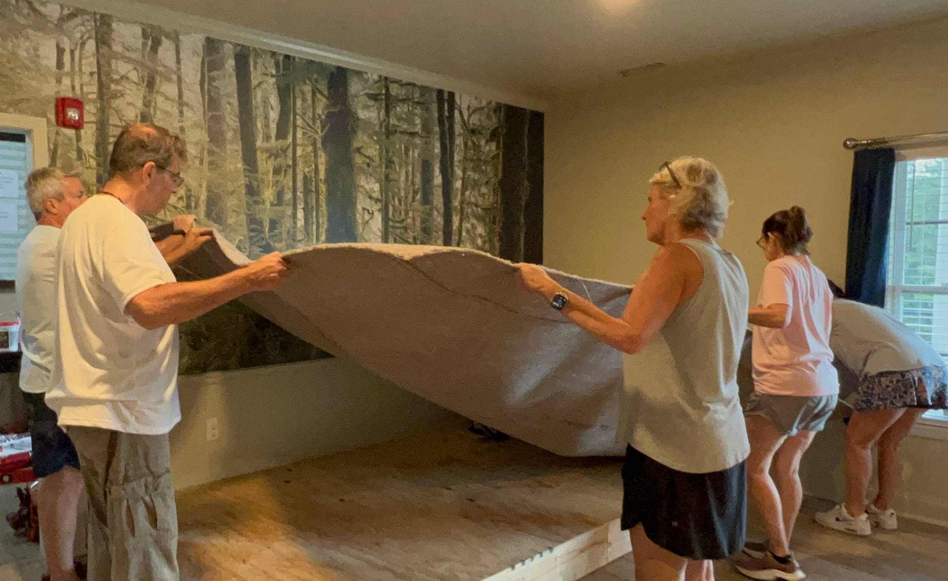 Volunteers carrying out old carpet padding in front of the forest mural wall during demolition.