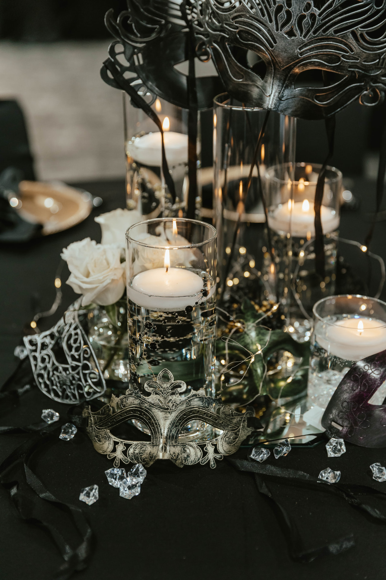 Table centerpiece of masquerade masks, floating candles and white roses.