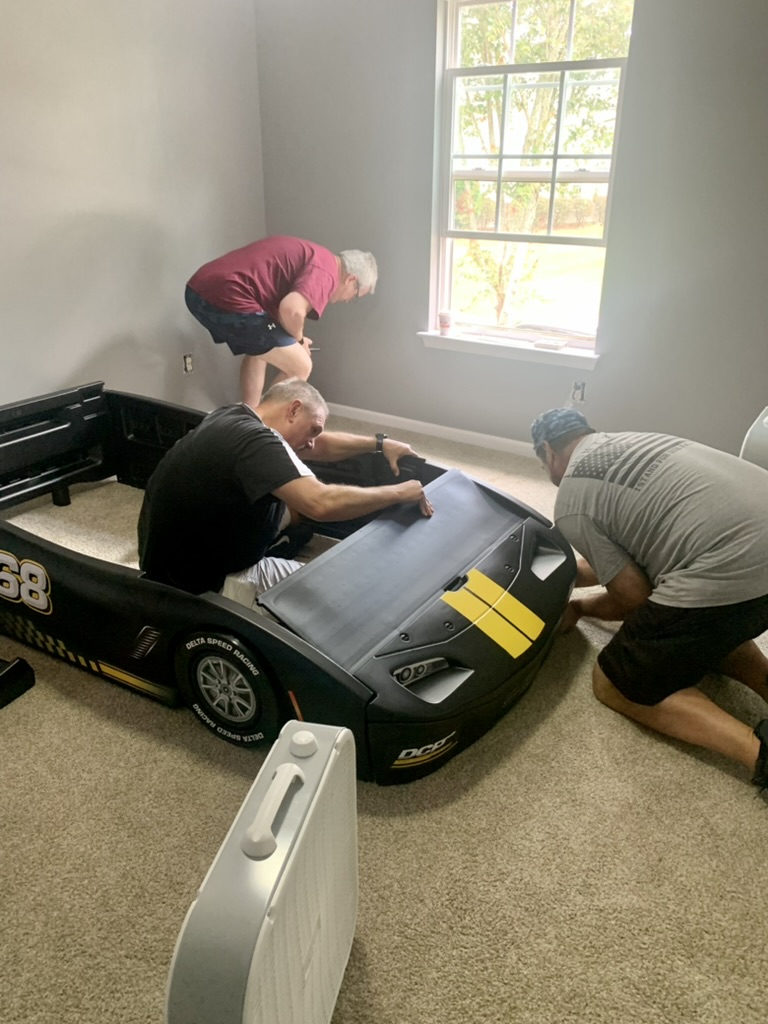 Volunteers assembling a car-shaped bed.