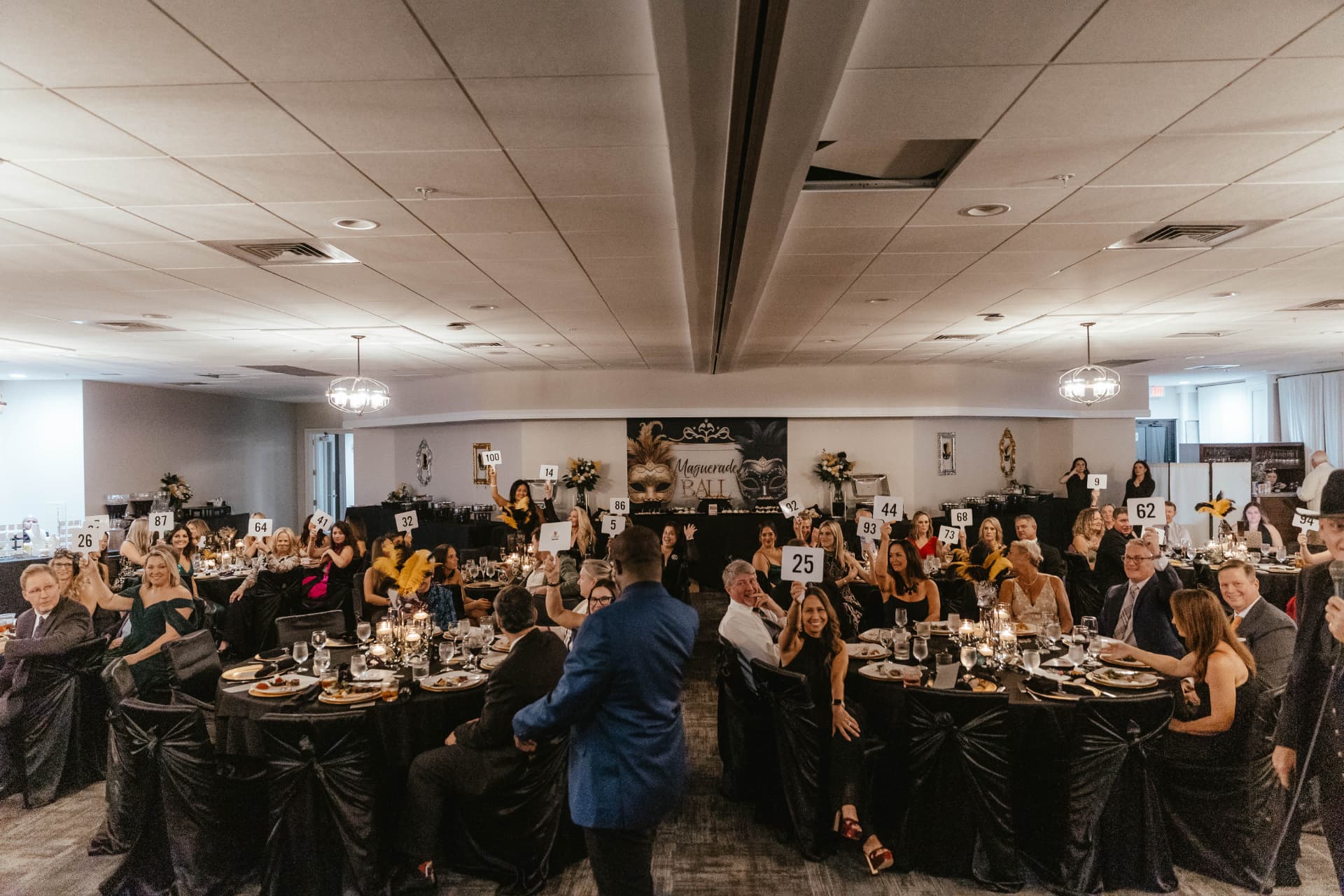 Gala guests seated at candlelit tables raising bidder paddles during the live auction.