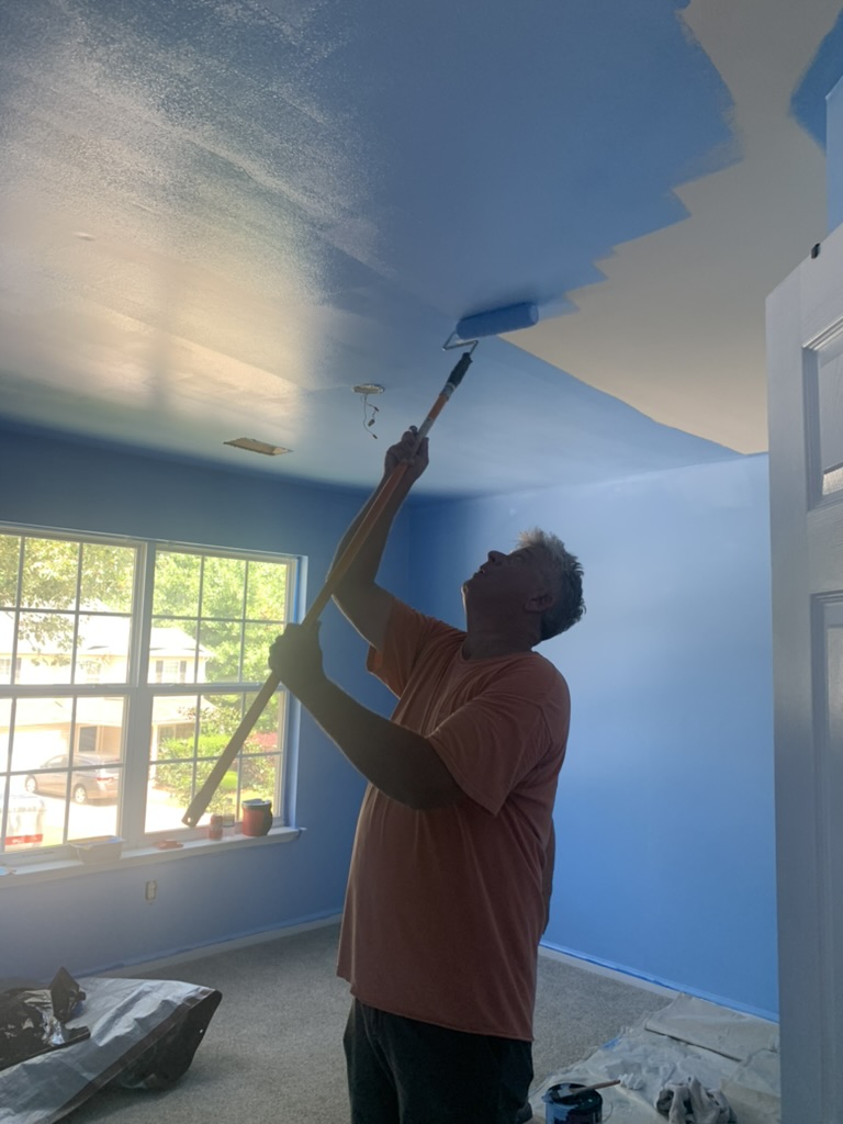 Volunteer painting a bedroom ceiling blue.
