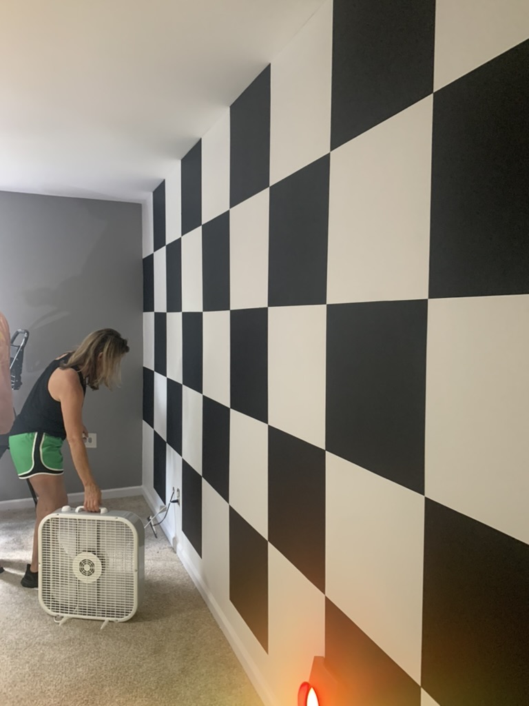 A freshly painted black and white checkered accent wall drying inside a bedroom.
